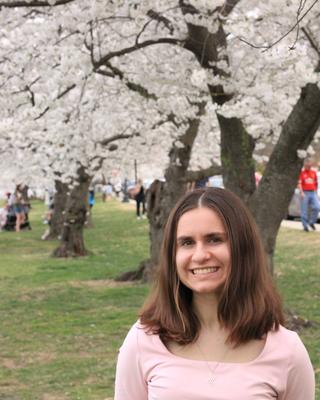 Woman with brown hair smiling in front of cherry blossoms