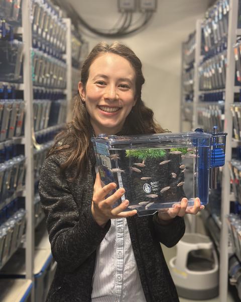 Smiling Woman with long hair holding a small tank with zebrafish